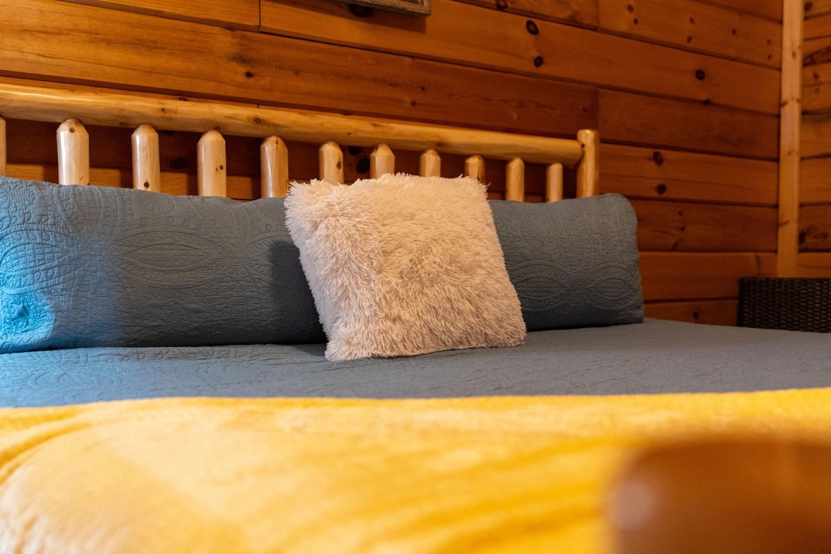 Una cama con cabecera de madera, dos almohadas y una colcha.