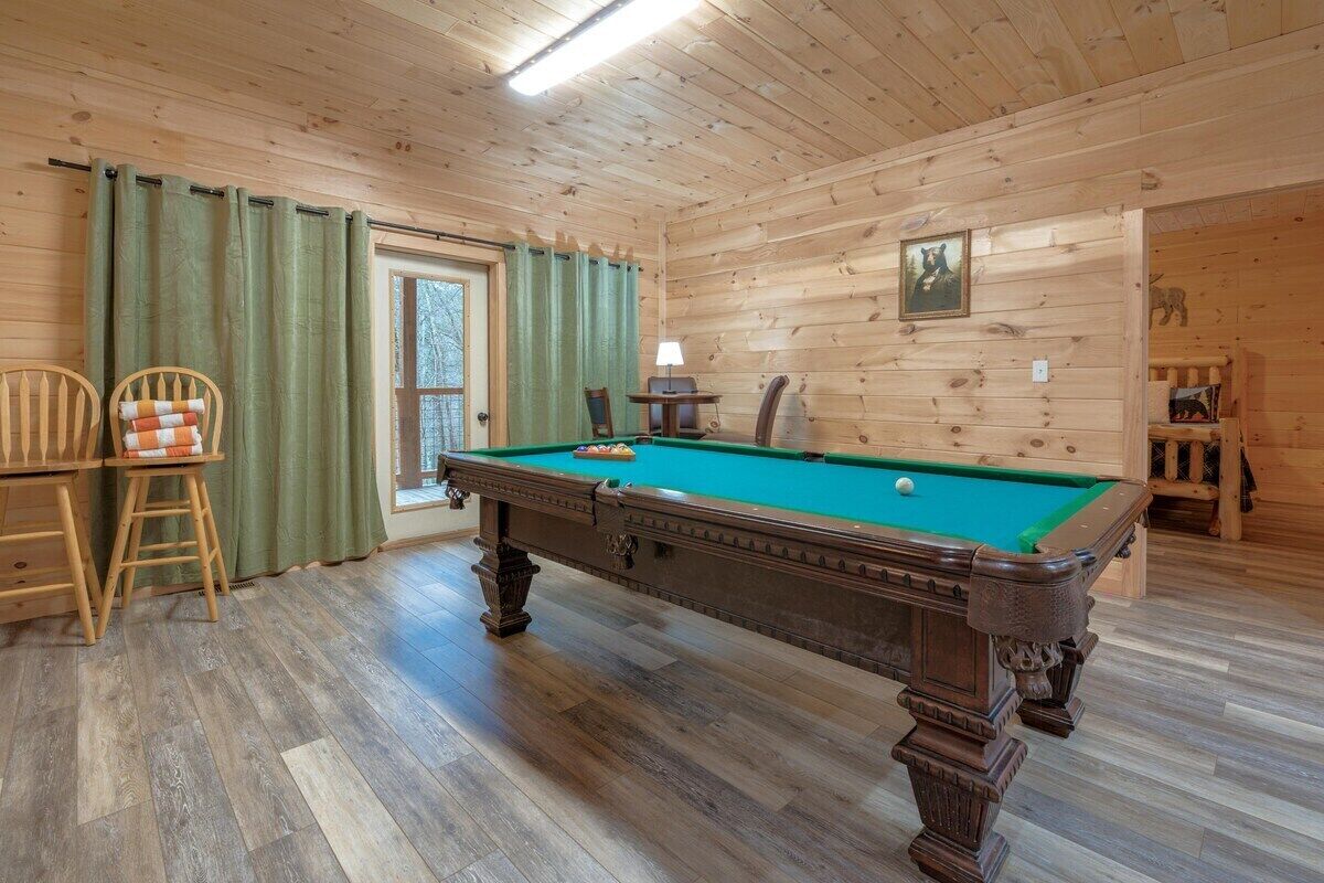 A wooden-paneled room with a pool table, chairs, and a door leading outside.