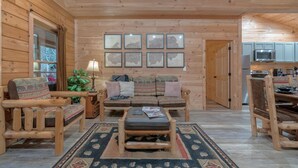 Een houten interieur met een bank, stoelen, een vloerkleed en ingekaderde kaarten aan de muur.