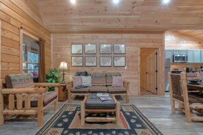 A wooden interior with a sofa, chairs, a rug, and framed maps on the wall. - Hot Tub & Dolly Tickets - Gatlinburg Cabin Retreat (Gatlinburg)