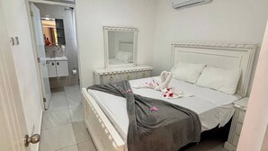 Ein Schlafzimmer mit Bett, Nachttischen, einem Spiegel und einem durch eine offene Tür einsehbaren Badezimmer.
