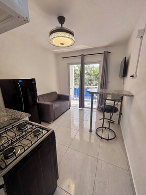 A modern kitchen with a gas stove, a refrigerator, a sofa, a dining table, and a ceiling light fixture. - Condo Neuf Avec Balcon Près de Tout à Sosua 206 (Sosúa)