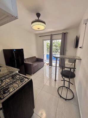 A compact kitchen with a gas stove, a refrigerator, a sofa, and a dining area with a table and chairs. - Condo Neuf Avec Balcon Près de Tout à Sosua 206 (Sosúa)
