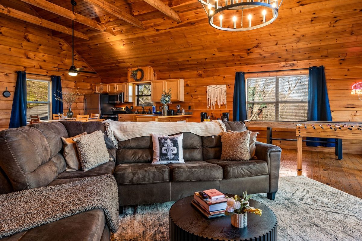 A cozy cabin interior with a leather sofa, a dining table, and a kitchen area.