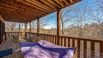 A wooden deck with a hammock and a hammock chair, overlooking a forested landscape.