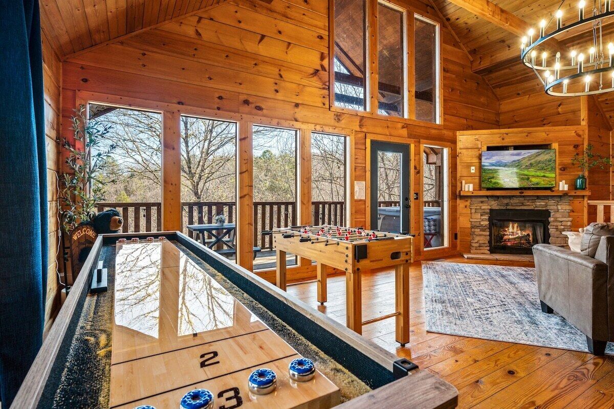 Une pièce au plancher de bois, équipée d’un baby-foot, d’une table de billard et d’une cheminée.