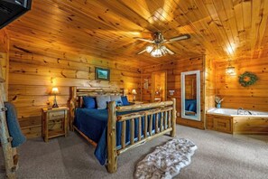 A log cabin bedroom with a wooden bed, a ceiling fan, a built-in bathtub, and a small rug. - Romantic, Hot Tub, Free Dollywood + Hot Spring Spa (Sevierville)