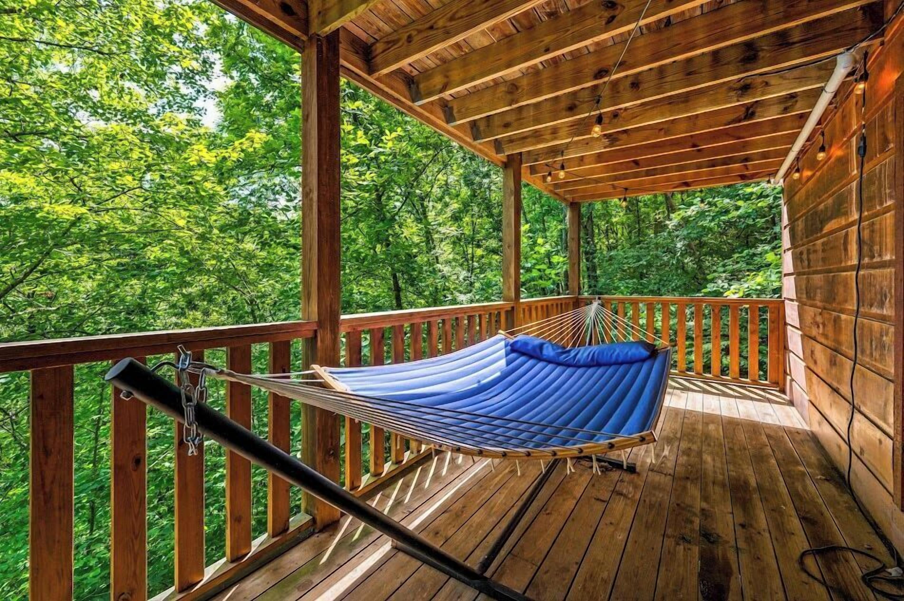 Une terrasse en bois avec un hamac et une balustrade donnant sur une forêt.