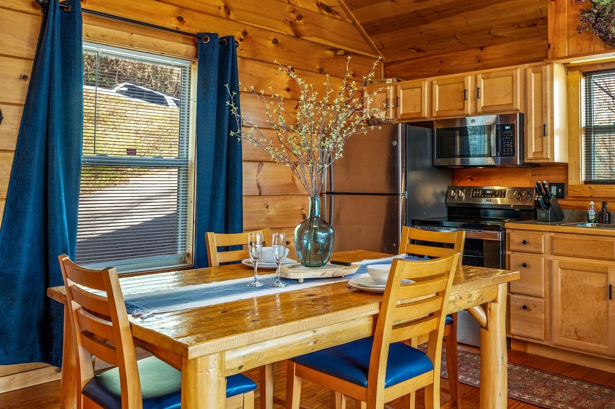 Interior de madera con una mesa de comedor, sillas, un florero con ramas, un microondas y un refrigerador.