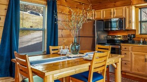 Un intérieur en bois comprenant une table à manger, des chaises, un vase avec des branches, un four à micro-ondes et un réfrigérateur.