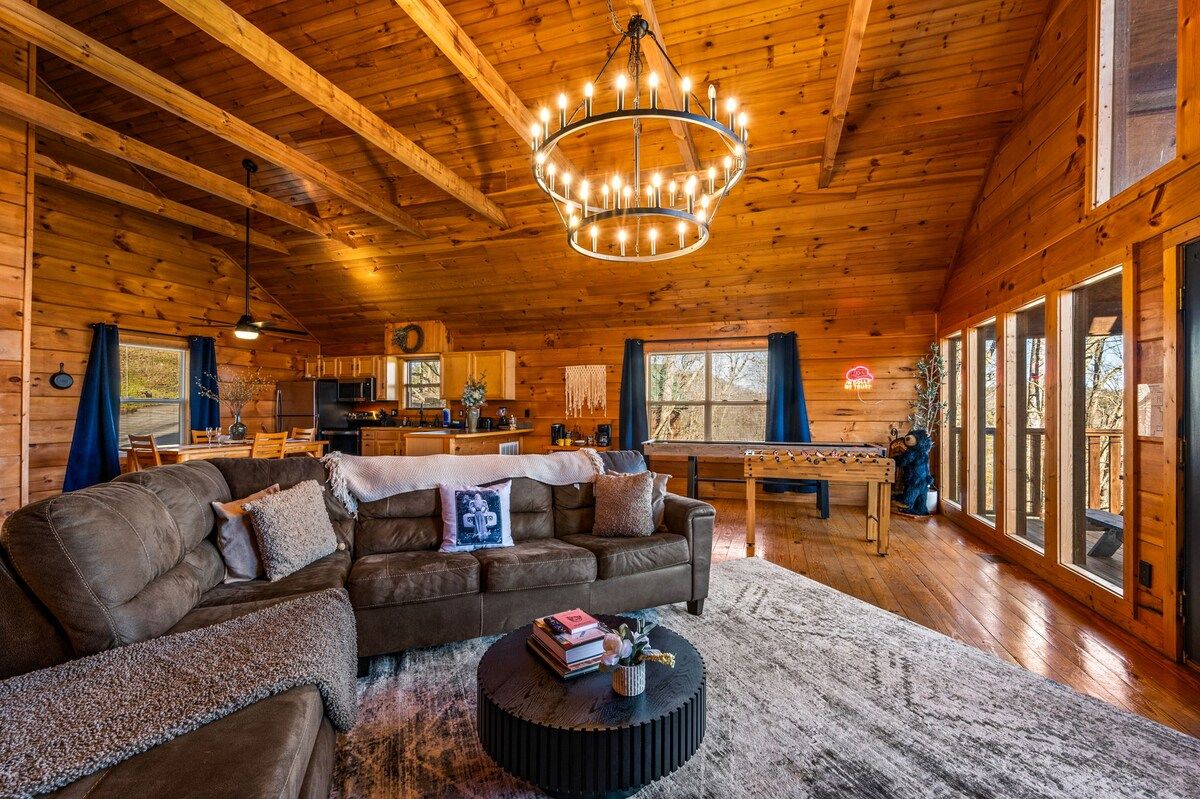 L’intérieur d’un chalet chaleureux, avec une grande table à manger en bois, un canapé et un lustre.