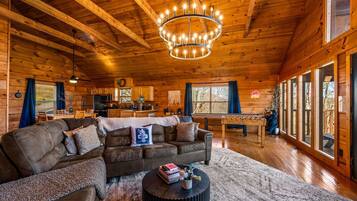 L’intérieur d’un chalet chaleureux, avec une grande table à manger en bois, un canapé et un lustre.