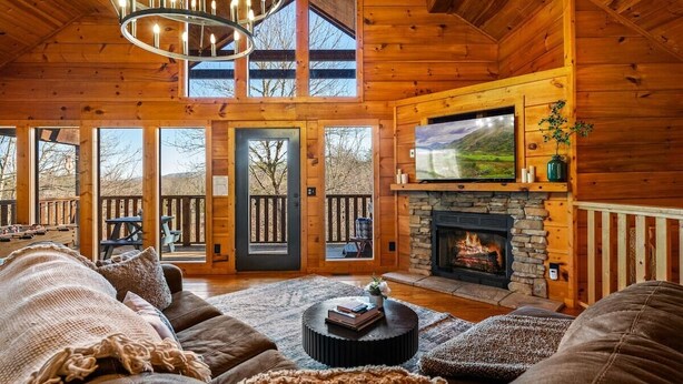 L’intérieur d’une cabane en rondins, avec une cheminée, un grand téléviseur et un coin salon confortable.
