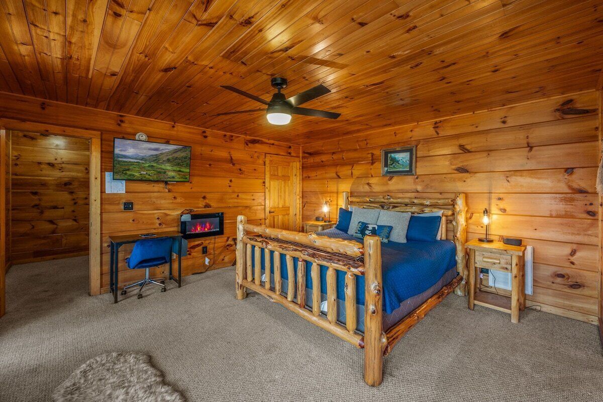 Une chambre dans une cabane en bois, comprenant un lit, un bureau, une chaise et un ventilateur de plafond.