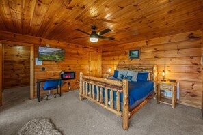 Een slaapkamer in een houten hut met een bed, bureau, stoel en een plafondventilator.