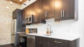 A modern kitchen with dark wood cabinets, stainless steel appliances, and a white countertop. - Spacious Exchange District Condo | 1 Bed | 1 Bath | (Winnipeg)
