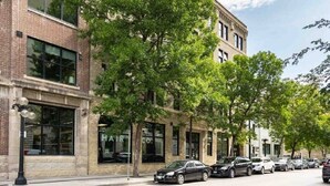 A street view with a row of parked cars, a building with large windows, and trees lining the sidewalk. - Spacious Exchange District Condo | 1 Bed | 1 Bath | (Winnipeg)