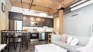 A modern kitchen with dark cabinets, stainless steel appliances, and a central island. - Spacious Exchange District Condo | 1 Bed | 1 Bath | (Winnipeg)