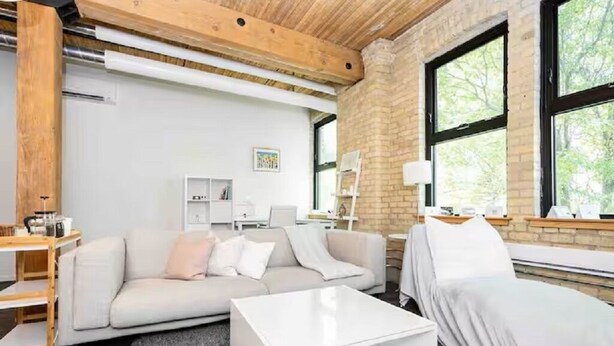 A modern living room with a sofa, a covered bed, a coffee table, and a desk with a lamp. - Spacious Exchange District Condo | 1 Bed | 1 Bath | (Winnipeg)