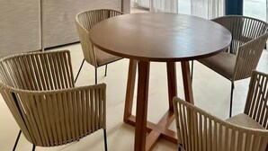 Ett modernt vardagsrum med ett runt träbord och flätade stolar, en grå soffa, en takfläkt och ett stort fönster med tunna, genomskinliga gardiner.