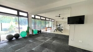 Ett rymligt gym med träningsutrustning, stora fönster och en platt-TV.