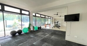 Ein großzügiger Fitnessraum mit Trainingsgeräten, großen Fenstern und einem Flachbildfernseher.
