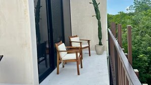 En balkong med en sittplats, en krukväxt i form av en kaktus och utsikt över grönområden.