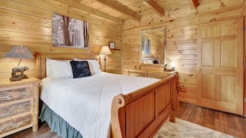 Ein Schlafzimmer einer Holzhütte mit einem Bett, Nachttischen, einem Spiegel und einer Tür.