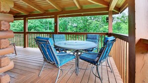 Un espace extérieur abrité, aménagé avec une table ronde et des chaises bleues, entouré d’une terrasse en bois et d’une clôture en bois.