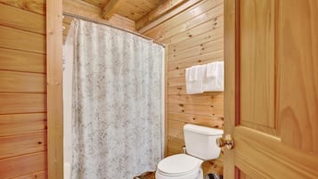 Ein Badezimmer mit Holzvertäfelung, einer Toilette, einer Duschvorhang und einem Handtuchhalter.
