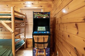 Uma cama de solteiro com escada de madeira, uma escrivaninha de madeira com um computador e uma janela com persianas.