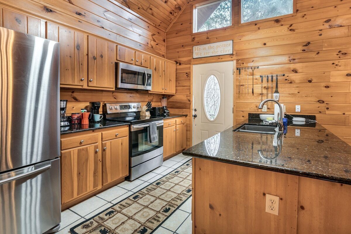 A wooden cabin kitchen with a stainless steel refrigerator, microwave, stove, and sink.