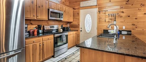Une cuisine rustique aménagée dans une cabane en bois, avec un réfrigérateur, un four à micro-ondes, une cuisinière et un évier en acier inoxydable.