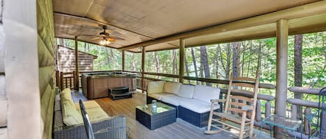 A covered outdoor seating area with a sofa, chairs, and a hot tub.