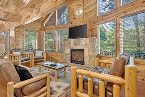 A log cabin interior with a fireplace, wooden furniture, and large windows. - Free Dollywood, Hot Tub, Firepit, Pool Table, Spa (Gatlinburg)