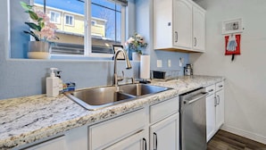 Una cocina con encimera de granito, pileta de acero inoxidable, muebles blancos y lavavajillas.