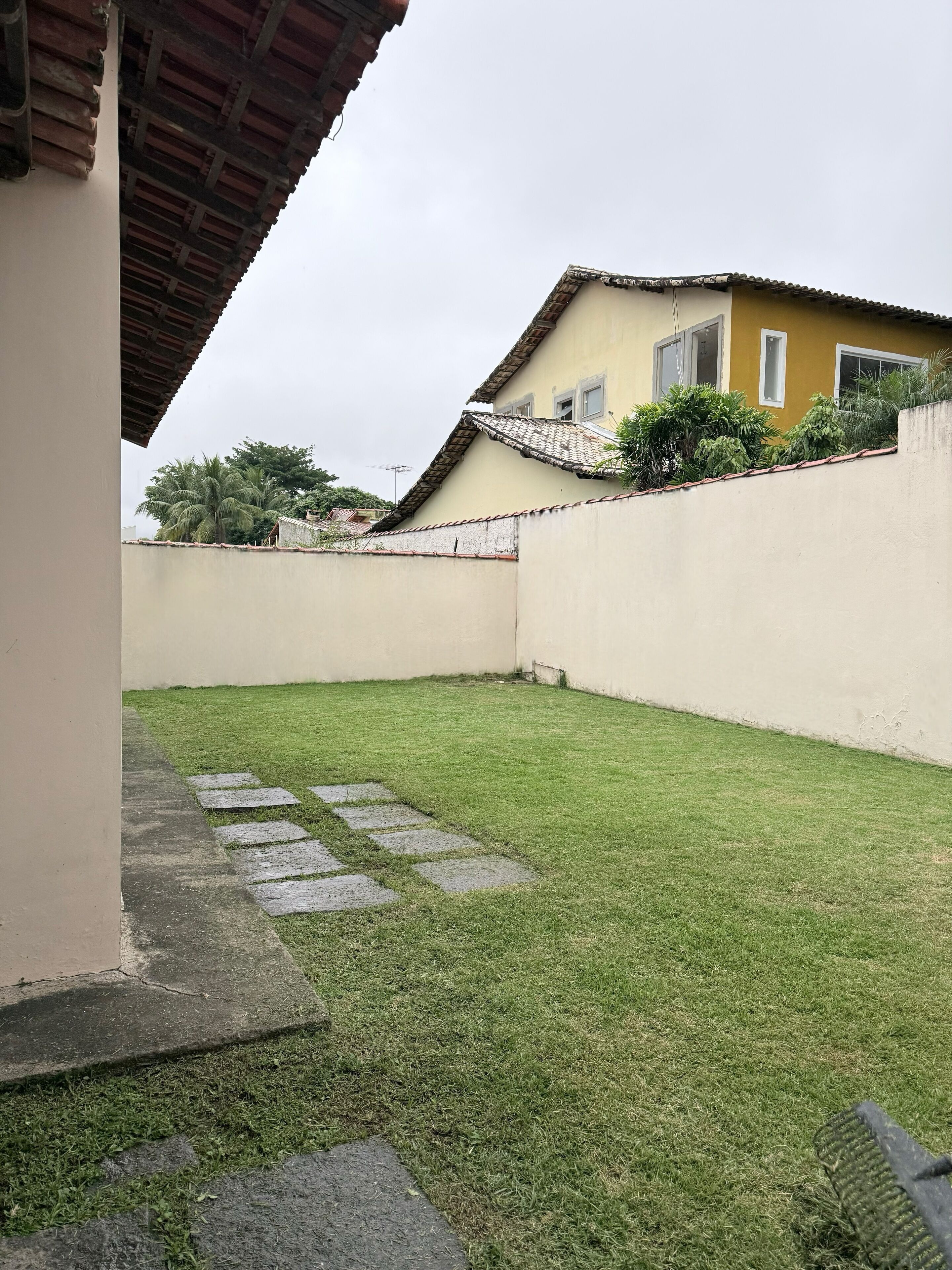 A well-maintained grassy yard with a stone pathway leading to a building with a tiled roof and a yellow wall.