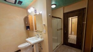 A bathroom with a toilet, sink, mirror, and glass shower enclosure.