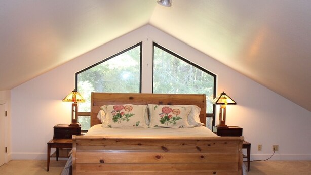 A bedroom with a wooden bed, two bedside lamps, and a large window.