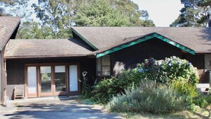 A two-story house with a covered porch, large sliding glass doors, and a garden with various plants and flowers.