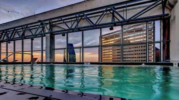 En pool med udsigt til en moderne bygning og en solnedgang.