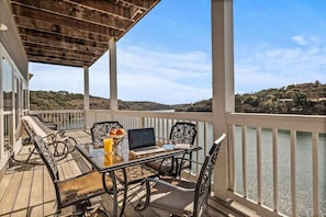 A covered outdoor deck with a table, chairs, and a laptop. - Lakefront Dream/Sleeps 16+/Pool/HotTub/Slides/Dock (Marble Falls)