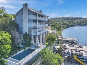 A multi-story building with balconies, a pool, and a dock extending into a body of water. - Lakefront Dream/Sleeps 16+/Pool/HotTub/Slides/Dock (Marble Falls)