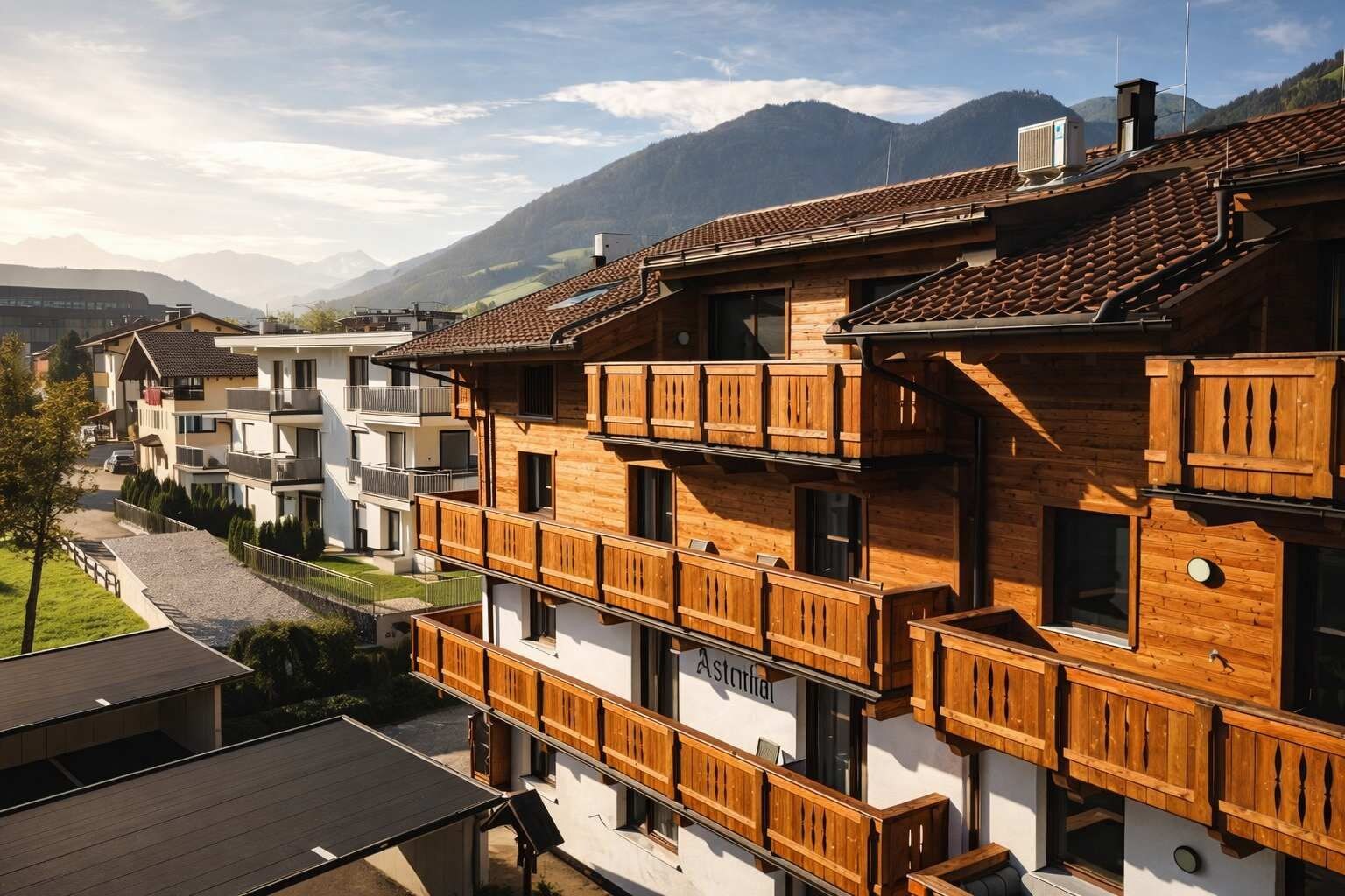 A multi-story building with wooden balconies, a ski slope in the background, and a mountain range.