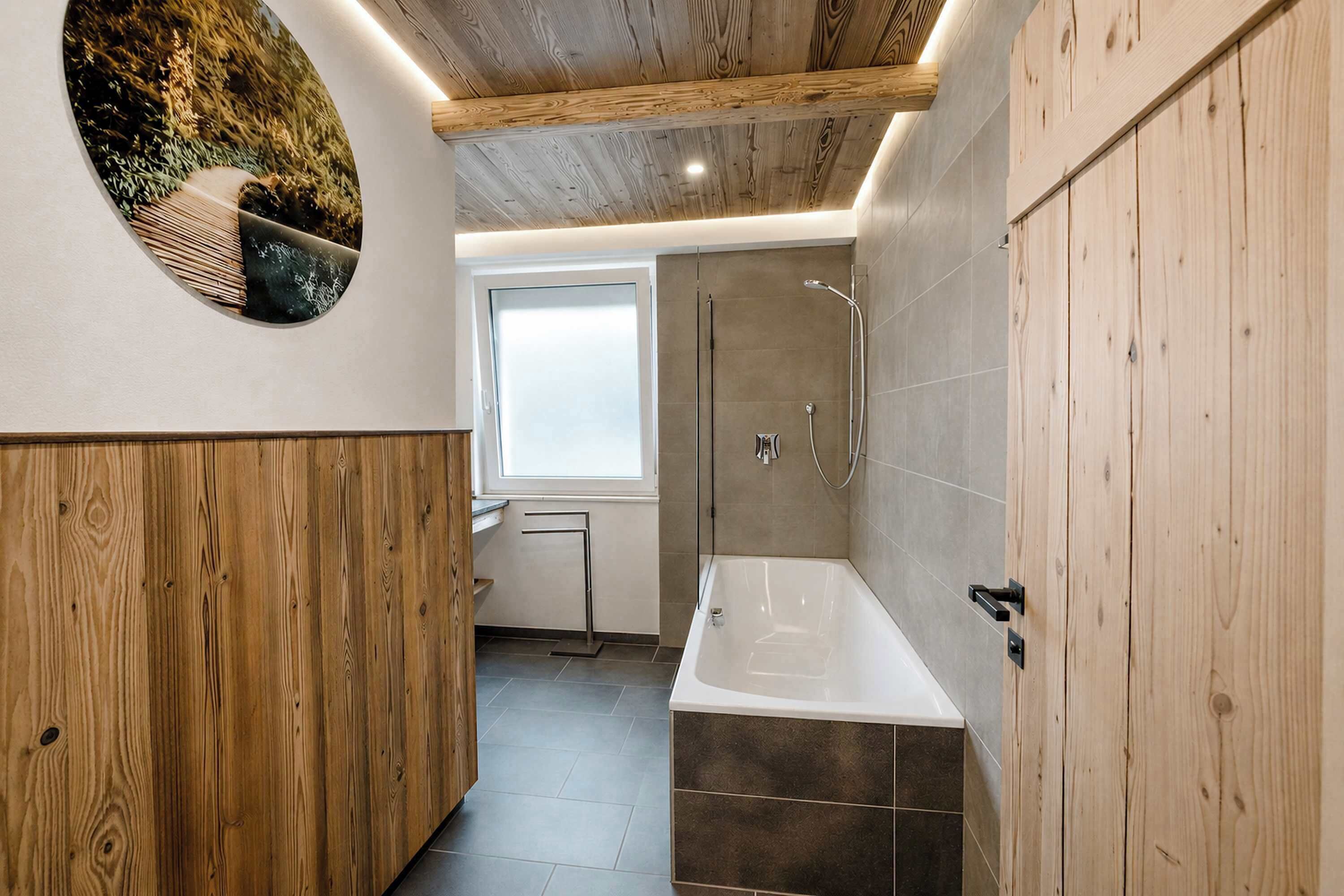 A modern bathroom with a wooden ceiling, a large circular mirror, a bathtub, and a shower area.