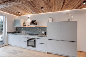 Une cuisine moderne avec des poutres en bois au plafond, un four encastré et un grand réfrigérateur.