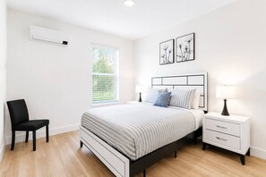 A bedroom with a bed, bedside tables, a chair, a window with blinds, and wall art. - Prime Suite by Convention Center and Bathhouse Row (Hot Springs)
