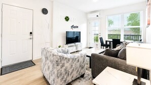 Un salon moderne comprenant un téléviseur, un canapé, une table basse et un coin repas avec une table et des chaises.