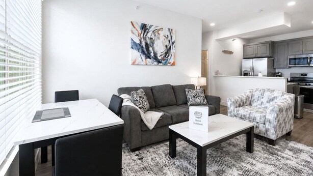 Un salon moderne avec un canapé, une table basse et une table à manger. On aperçoit à l’arrière-plan un coin cuisine avec des placards et des appareils électroménagers.