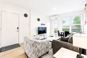 A modern living room with a television, a sofa, a coffee table, and a dining area with a table and chairs. - Prime Suite by Convention Center and Bathhouse Row (Hot Springs)